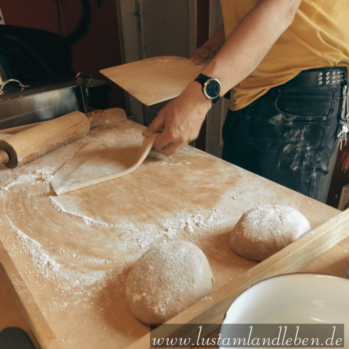 Pizzateig auf dem Backtisch. Mann rollt Pizza aus in schwarze Jeans mit Nietengürtel.