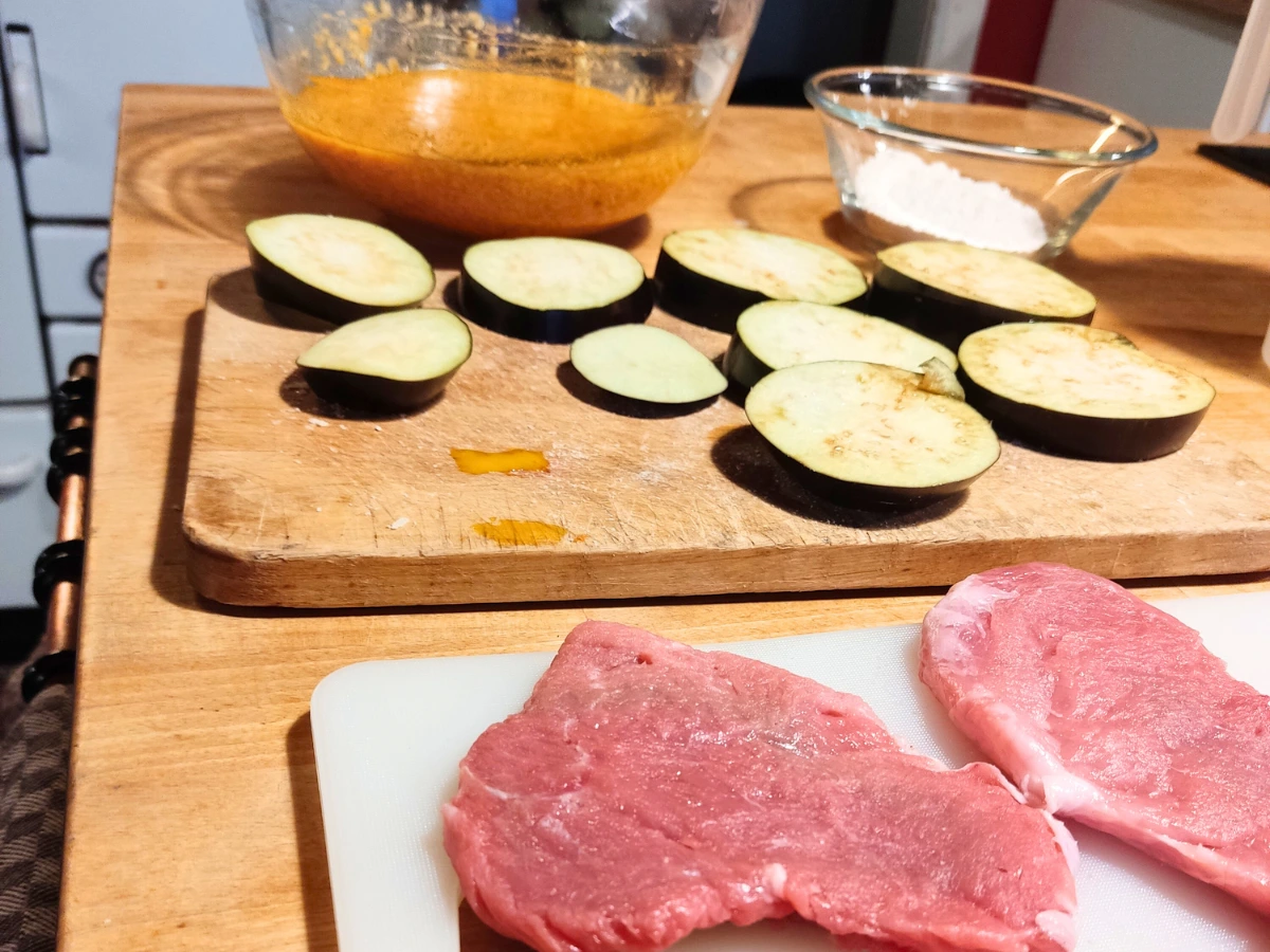 Fleisch und Auberginen panierbereit auf Küchenbretter