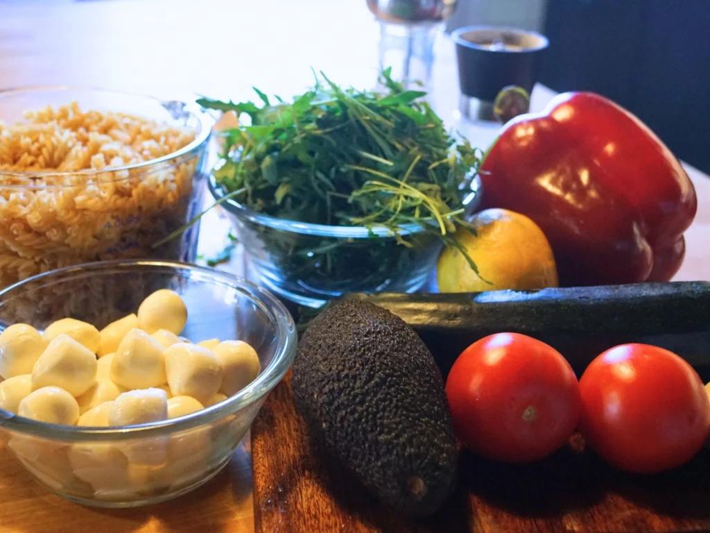 Frühlingsnudelsalat mit Avocado, Mozzarella und Rucola zutaten auf Holzbrett