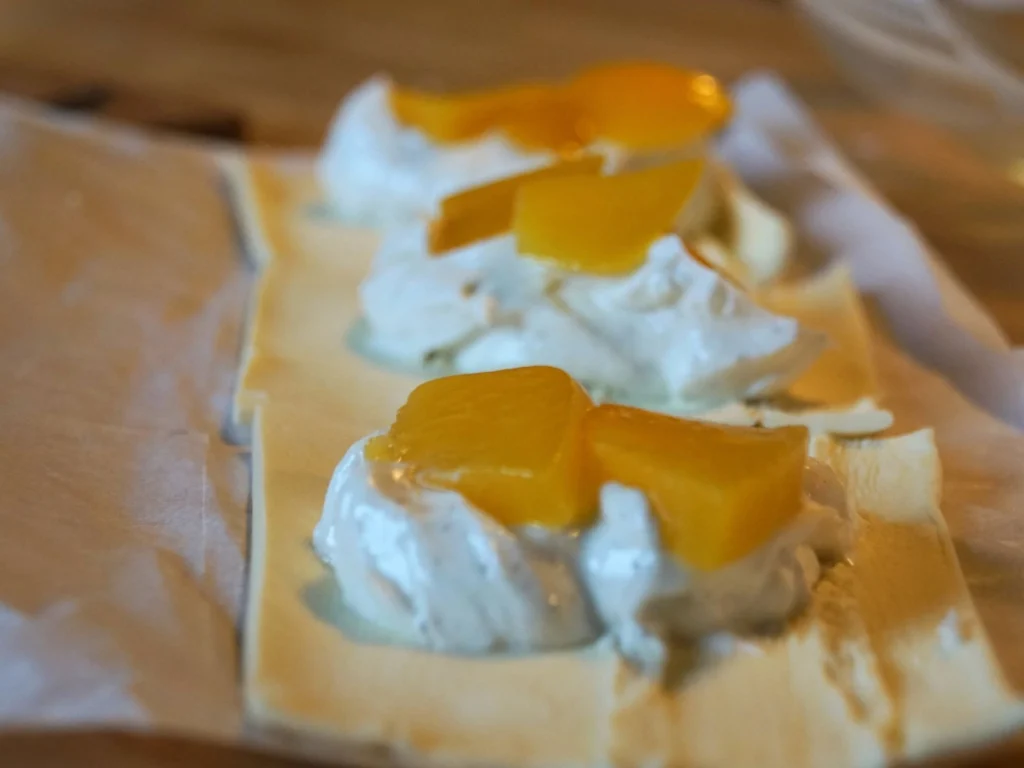 Blätterteig mit einem Klecks Quark und Pfirsisch in Scheiben auf Backpapier