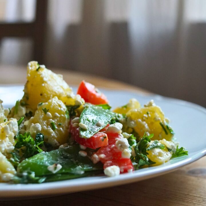 Kartoffelsalat mit Zuckererbsen und Paprika auf einem Weißen Teller am Holztisch