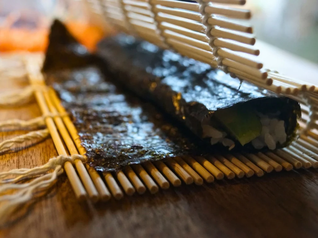 Sushirolle wird mit Bambusmatte zusammengerollt